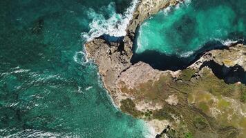 Overhead perspective reveals dynamic colors of swirling ocean waters colliding with rocks, creating stunning close-up of picturesque rocky shoreline video