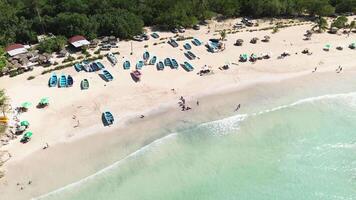 Aerial view of sunny day on tropical beach, showcasing clear waters, fishing boats along shore, and tourists relaxing and having good time. Background. Space for text. Abstraction. Flying forward video