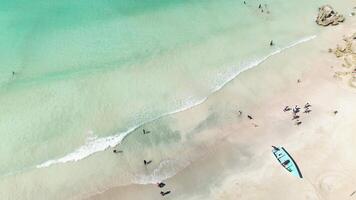 Minimalist composition featuring fishing boat moored by tropical coastline, contrasted with vibrant scene of tourists delighting in clear turquoise waters. Dominican Macao Beach, space for text video