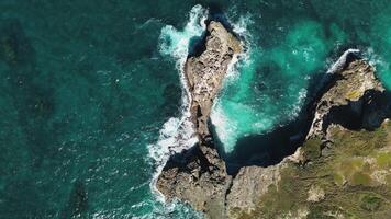 aéreo topo Visão do ondas falhando para rochoso afloramentos dentro sereno azul oceano. isto aéreo cenas vitrines beleza do oceano ondas encontro deserta rochoso penhasco a partir de olho do pássaro visualizar. espaço para texto video