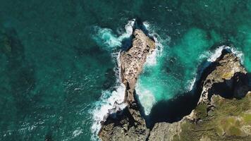 närbild se av en pittoresk klippig kustlinje fångar de vibrerande nyanser av hav vattnen virvlande och vågor kraschar mot de rocks. Drönare kamera övergångar till de gränslös hav. topp se video