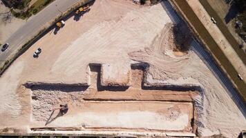 Aerial top view of construction site shows dug-out area for building foundation, with heavy machinery bustling around. This location is situated in Vistacana, Punta Cana, Dominican Republic. Zoom out video