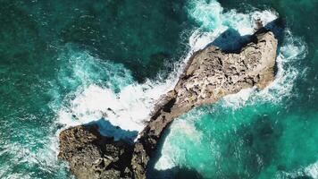 aereo Visualizza di vivace tonalità di vorticoso oceano acque e Crashing onde contro il rocce siamo catturato nel un' avvicinamento Visualizza di un' pittoresco roccioso costa video