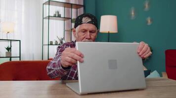 mayor antiguo abuelo empieza trabajando en computadora portátil, envía mensajes, hace en línea compras a hogar video
