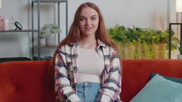 Young woman smiling friendly at camera, waving hands gesturing hello, hi, greeting at home on sofa video