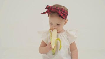 pequeno menina dentro xadrez arco de cabelo é comendo banana video