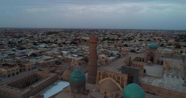 das Drohne fliegt um das Minarett von das architektonisch Komplex poi-kalon. im das Hintergrund sind das alt Häuser von Buchara, Usbekistan. früh wolkig Morgen video