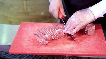 açougueiro fatiamento carne de porco para culinária preparação, açougueiro dentro luvas precisamente corte cru carne de porco em uma vermelho corte borda. video