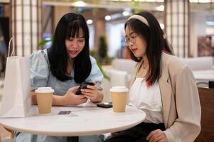 Two Asian female friends are enjoying talking while sitting together in a cafe in the shopping mall. photo