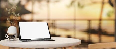 A digital tablet mockup on a round table with a blurred background of a sunset beach view. photo