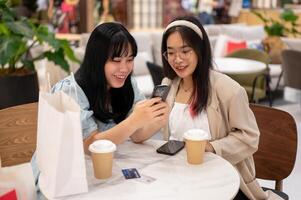 Two Asian female friends are enjoying talking while sitting together in a cafe in the shopping mall. photo