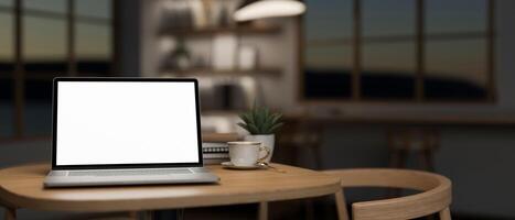 A laptop computer mockup on a wooden table in a minimalist comfortable coffee shop at night photo