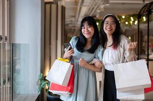 Two joyful Asian women holding shopping bags in a shopping mall, having a fun shopping day together. photo