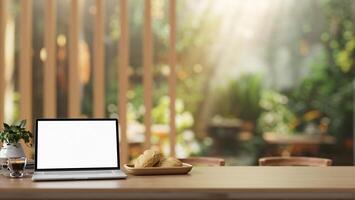 A laptop computer with a white screen mockup on a rustic wooden table in a beautiful cafe garden. photo
