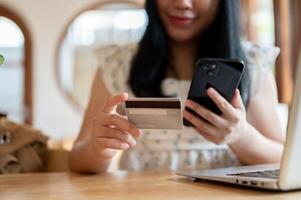 An Asian woman holding a credit card and a smartphone while sitting at a table in a cafe. photo
