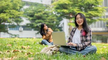 A female student is sitting on the grass in a park on a sunny day, using a laptop for studying. photo