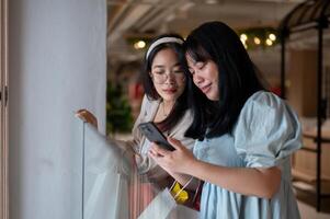 Two Asian women chat happily in a shopping mall corridor, looking at a smartphone together. photo