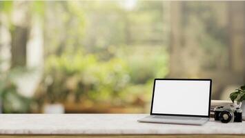 A laptop computer mockup on a white tabletop with a blurred background of a green garden. photo