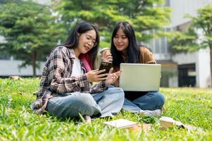 Two college students are sitting on grass in a park, discussing something on a smartphone together. photo