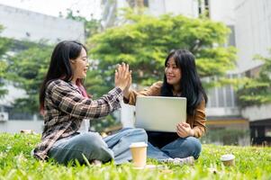 Two cheerful college students are giving each other a high five while sitting on the grass in a park photo