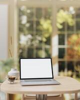 A laptop computer mockup and a coffee cup are placed on a wooden table in a beautiful coffee shop. photo