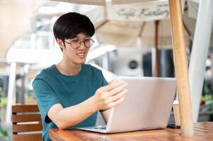 A man is working remotely, working on his laptop while sitting at an outdoor table of a cafe. photo