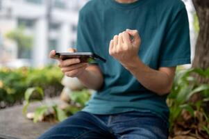 A cropped image of a man in casual wear showing his fist, playing a mobile game outdoors. photo