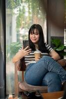 A woman relaxing in a cafe, using her smartphone and enjoying her coffee at a table by the window. photo