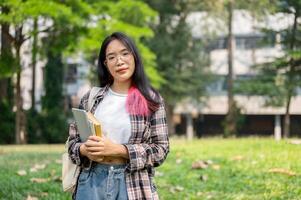 A confident young Asian female college student is looking at the camera while standing in the park. photo