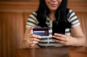 A cropped image of an Asian woman holding a smartphone and a credit card at a table in a coffee shop photo