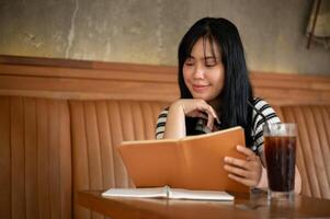 A happy young Asian woman is reading a book or doing homework in a beautiful vintage coffee shop. photo