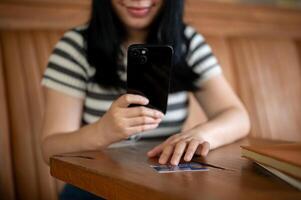 un mujer registrando su crédito tarjeta en un compras aplicación en su móvil teléfono, sentado en un cafetería. foto