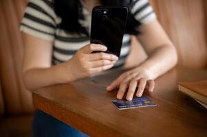 un mujer registrando su crédito tarjeta en un compras aplicación en su móvil teléfono, sentado en un cafetería. foto