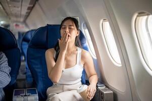 A female passenger is feeling tired and sleepy during a long flight, while traveling by plane. photo