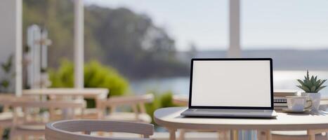 A laptop computer mockup on a table in a beautiful contemporary cafe or restaurant by the beach. photo