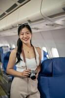 An attractive Asian female passenger stands in the aisle on a plane, smiling at the camera. photo