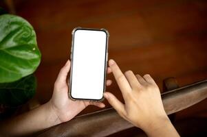 A close-up image of a woman using her smartphone indoors. A white-screen smartphone mockup photo