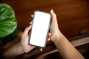 A woman holding a white-screen smartphone mockup over a blurred rustic wood background. photo