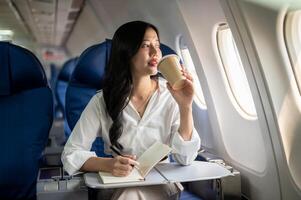 An elegant Asian businesswoman is sipping coffee while looking at the view outside the plane window. photo