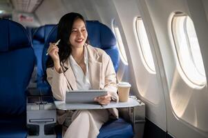 un exitoso asiático mujer de negocios es sentado a un ventana asiento en un avión con su digital tableta. foto