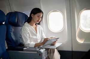 An attractive, hard-working Asian businesswoman is working on her tablet while traveling by plane. photo