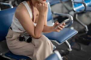 un hembra viajero utilizando su teléfono inteligente mientras sentado a un esperando asiento en el aeropuerto Terminal. foto