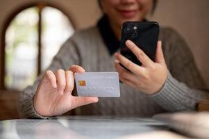 A cropped image of a satisfied Asian woman shopping online via her smartphone while sitting indoors. photo