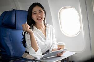 A confident Asian businesswoman is sitting at a window seat on a plane with her digital tablet. photo