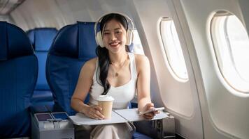 An attractive Asian woman is enjoying music on her headphones during the flight, traveling by plane. photo