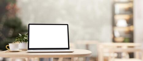 A white-screen laptop computer mockup on a wooden table in a cozy contemporary coffee shop cafe. photo