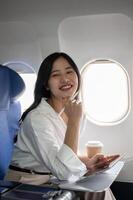 An attractive businesswoman is sitting in the window seat on a plane, traveling for a business trip. photo