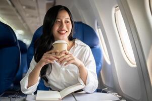 An elegant Asian businesswoman is sipping coffee while looking at the view outside the plane window. photo