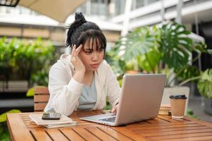 A serious, focused Asian woman is reading an online article or email on her laptop. photo