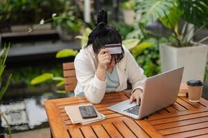 A upset Asian woman hand covering her face while holding a credit card, having financial problems. photo